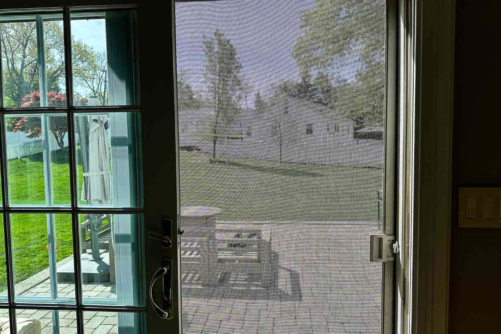 A bronze steel pet grille installed on a sliding patio screen door, protecting against pet scratches