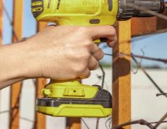 A person drilling pilot holes to install a pet grille on a swinging screen door