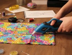 Person using cordless electric scissors to cut colorful fabric on a crafting table