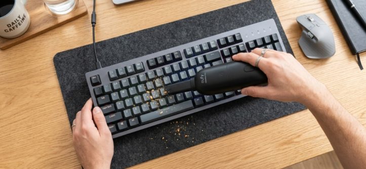 Person using a mini vacuum to clean a mechanical keyboard.